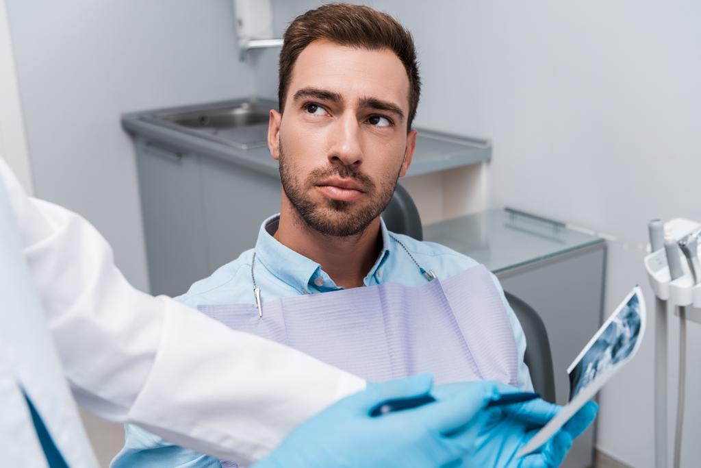 vue recadrée du dentiste tenant une radiographie près d'un beau patient
  - Photo, image
