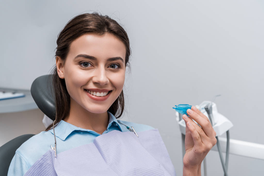 vrolijke vrouw met blauwe houder in tandheelkundige kliniek  - Foto, afbeelding