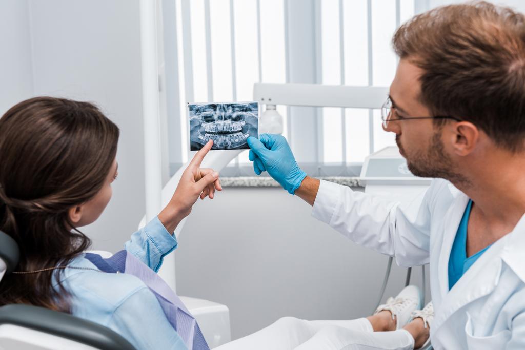 μούσι οδοντίατρος σε γάντι λατέξ κρατώντας ακτινογραφία κοντά στον ασθενή  - Φωτογραφία, εικόνα