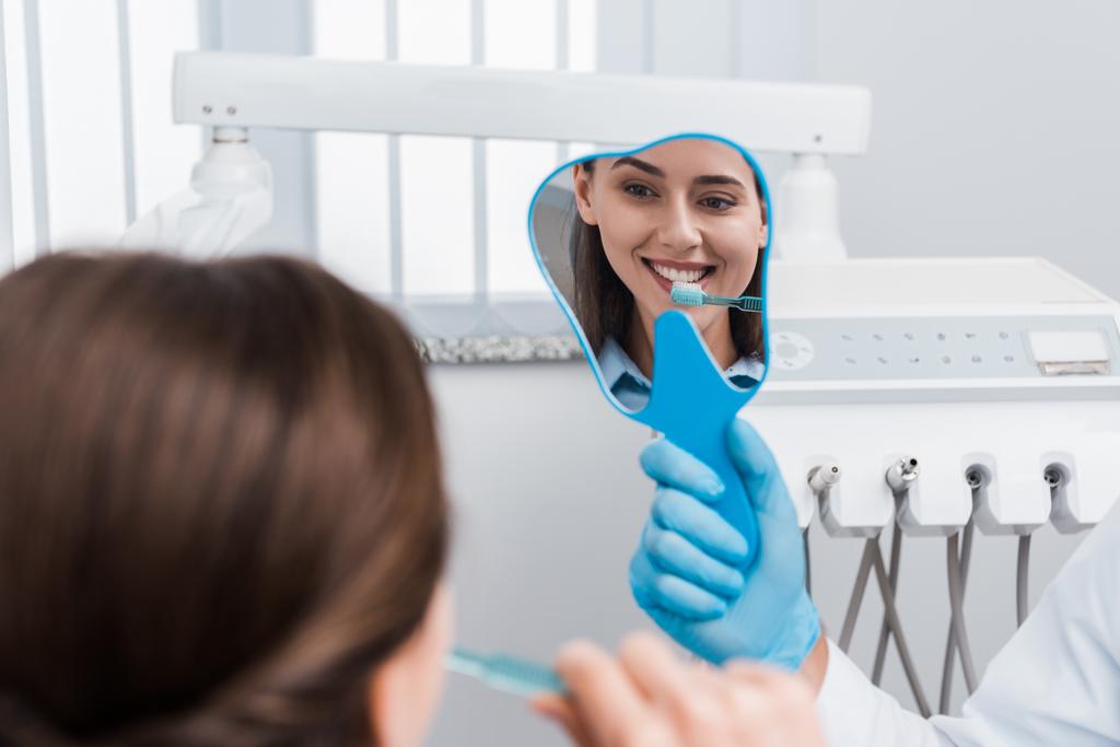 selektywnej ostrości dziewczyna szczotkowanie zębów i patrząc na lustro w pobliżu dentysty  - Zdjęcie, obraz