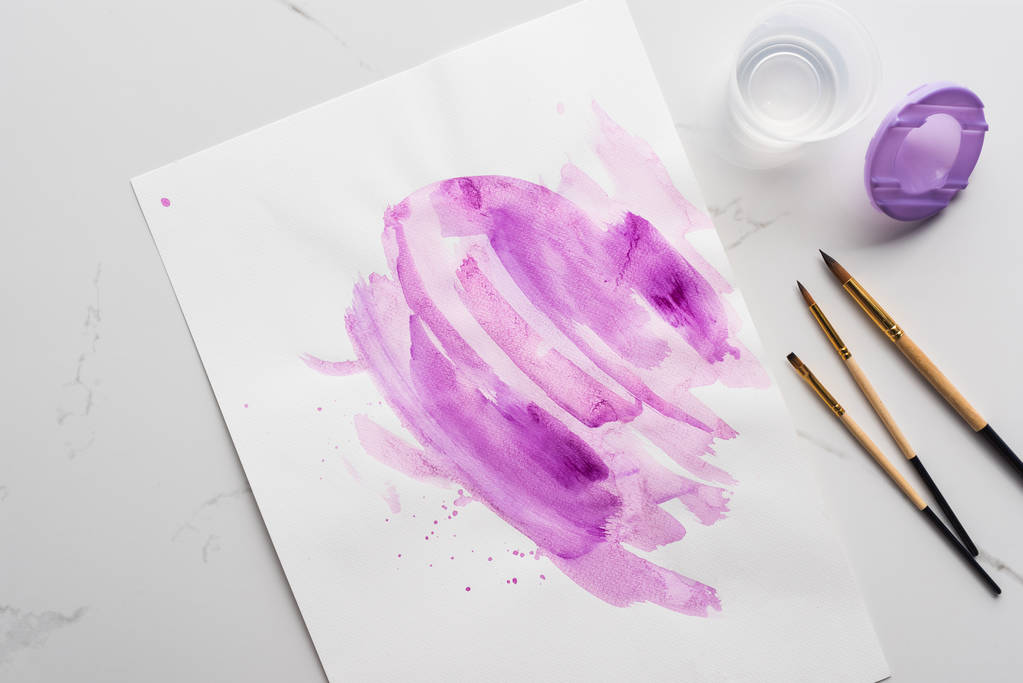 felülnézet lila akvarell ecsetvonásokkal a fehér papír közelében ecsetek a márvány fehér felület - Fotó, kép