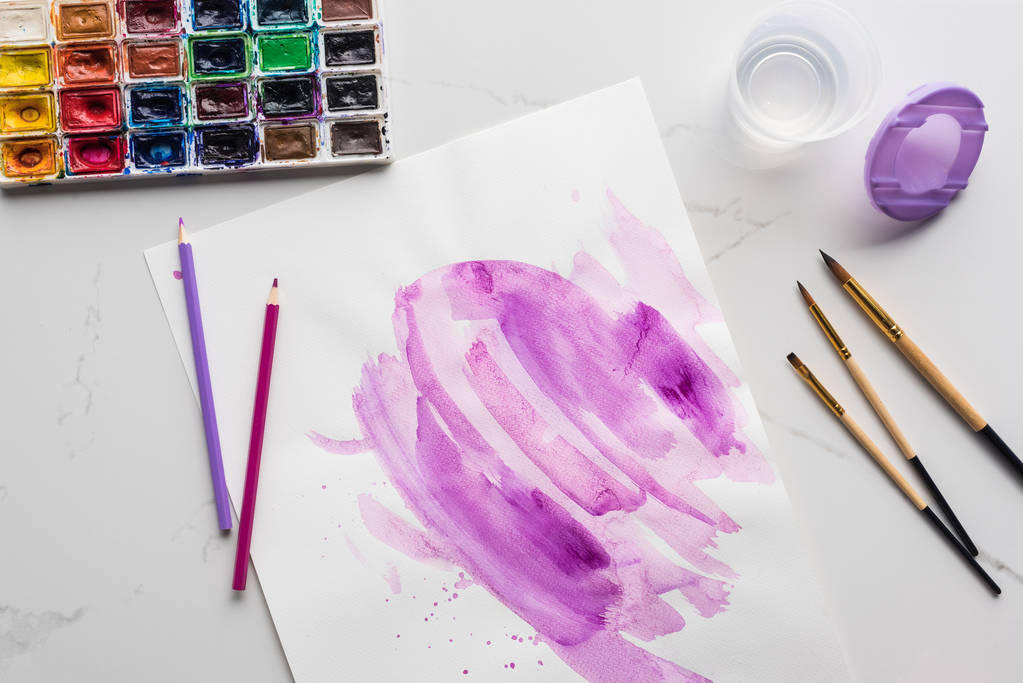 bovenaanzicht van Purple aquarel penseelstreken op wit papier in de buurt van penselen en verven op marmer wit oppervlak - Foto, afbeelding