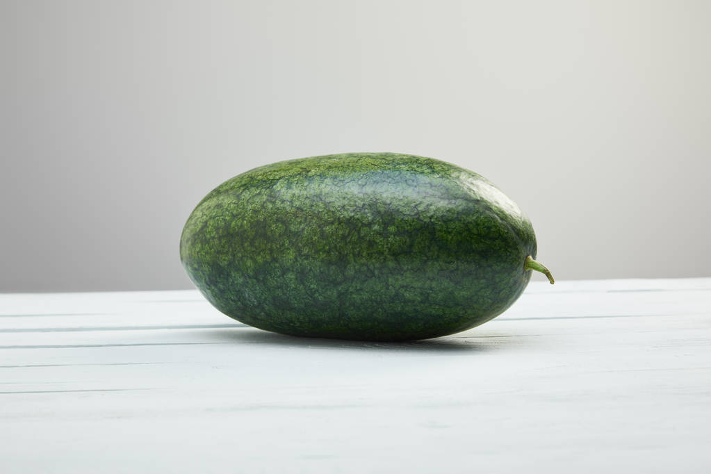 zelený celý meloun na bílém dřevěném stole izolovaný na šedé - Fotografie, Obrázek