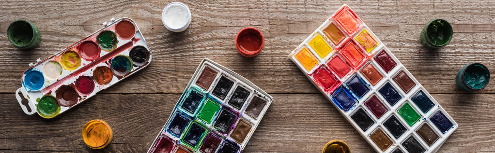 top view of colorful paint palettes on wooden brown table with gouache, panoramic shot - Photo, Image
