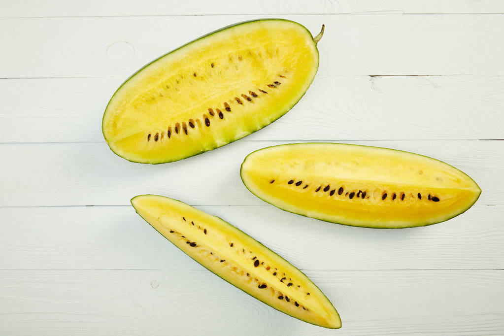 Draufsicht auf reife gelbe Wassermelone mit Samen auf weißem Holztisch - Foto, Bild