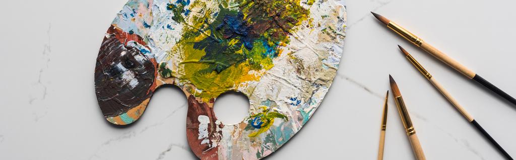 top view of colorful palette with oil paints near paintbrushes on marble white surface, panoramic shot - Photo, Image