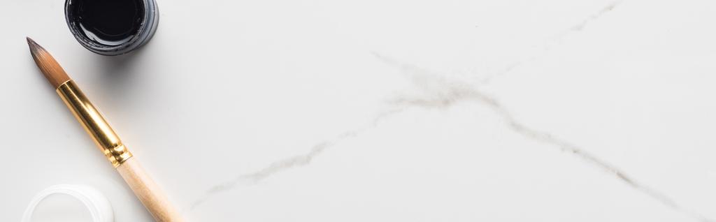 Draufsicht auf schwarz-weiße Gouachefarben und Pinsel auf marmorweißer Oberfläche, Panoramaaufnahme - Foto, Bild