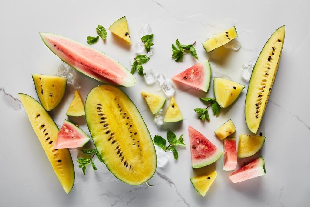 Draufsicht auf geschnittene köstliche exotische gelbe und rote Wassermelonen mit Eis und Minze auf Marmoroberfläche - Foto, Bild