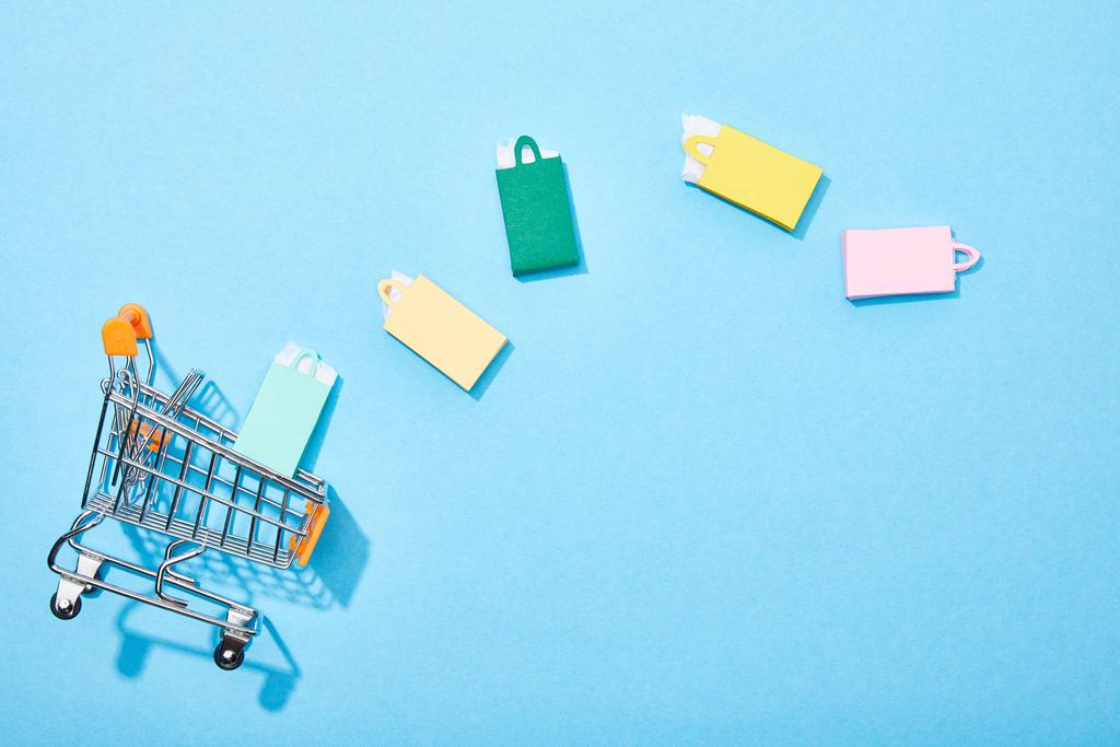 青のカラフルな紙袋の近くにおもちゃのショッピングカートのトップビュー  - 写真・画像