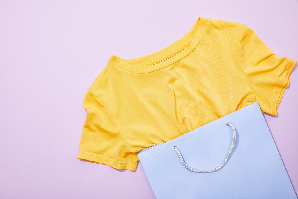 вид зверху на жовту футболку в фіолетовій торгової сумці на фіолетовому
  - Фото, зображення