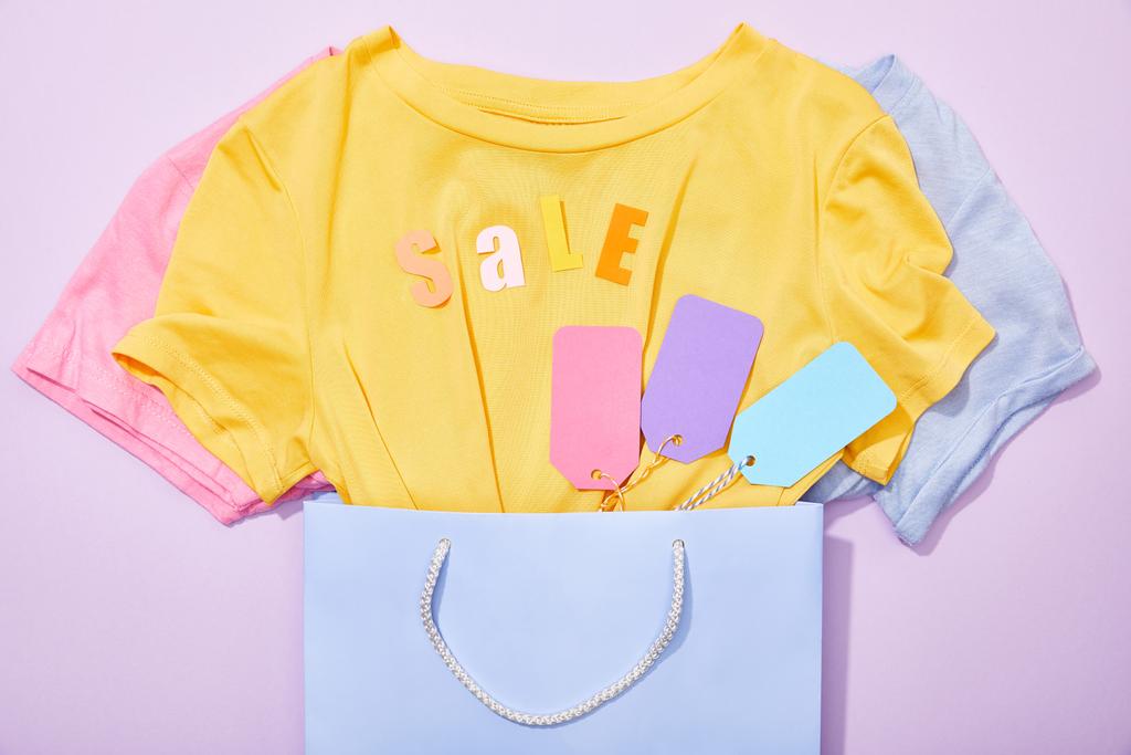 вид зверху на футболки з барвистими тегами в сумці для покупок на фіолетовому
 - Фото, зображення
