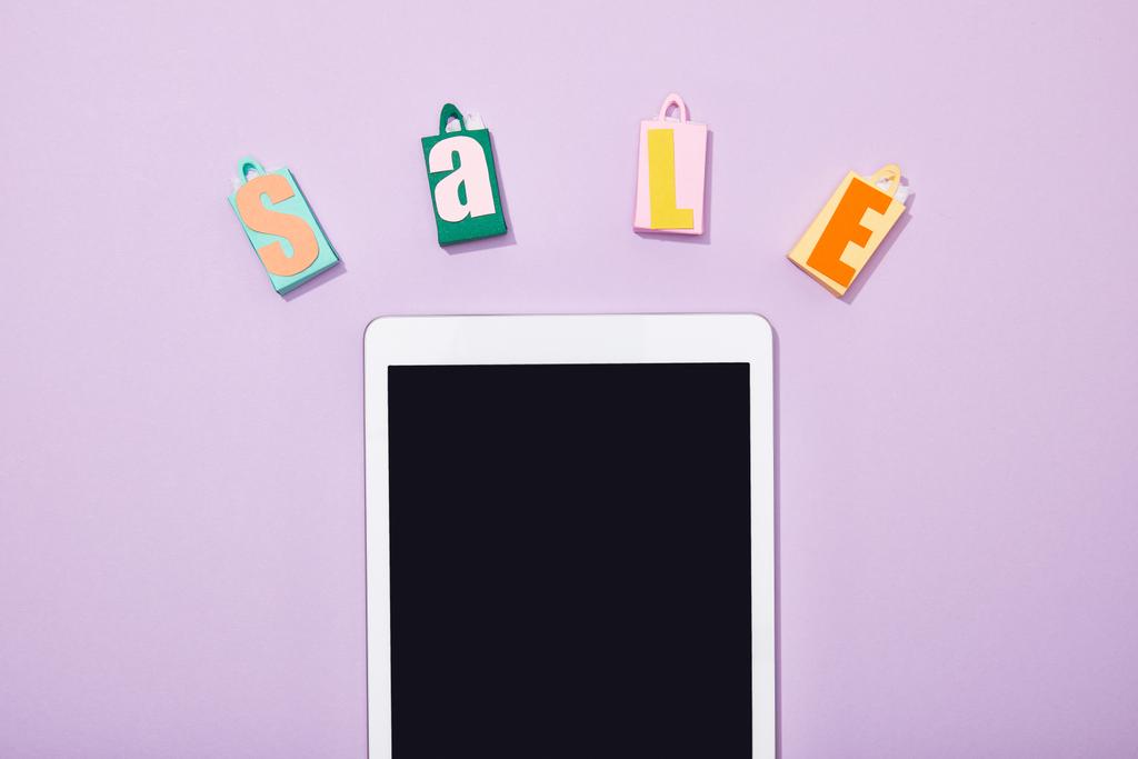 vista superior de bolsas de compras de papel con letras de venta cerca de la tableta digital con pantalla en blanco en violeta
  - Foto, imagen