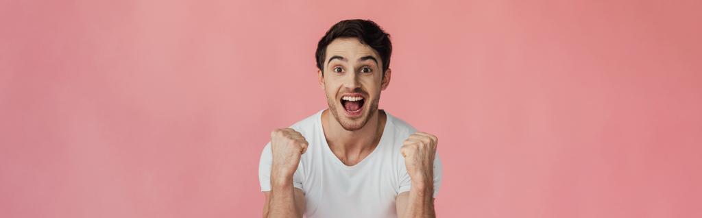 панорамный снимок взволнованного молодого человека, улыбающегося в камеру и показывающего жест "да", изолированный на розовом
 - Фото, изображение