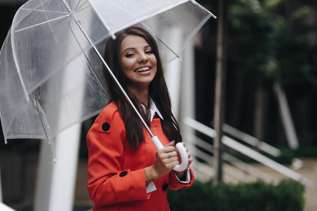 Concepto de negocios, clima y gente. Joven mujer de negocios europea sonriente con paraguas en la calle de la ciudad de primavera
. - Foto, Imagen