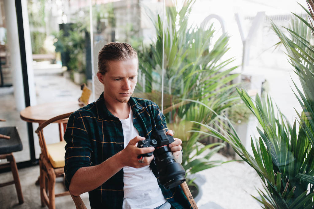 Photographe créatif tenant appareil photo professionnel, assis au café avec ordinateur portable
. - Photo, image
