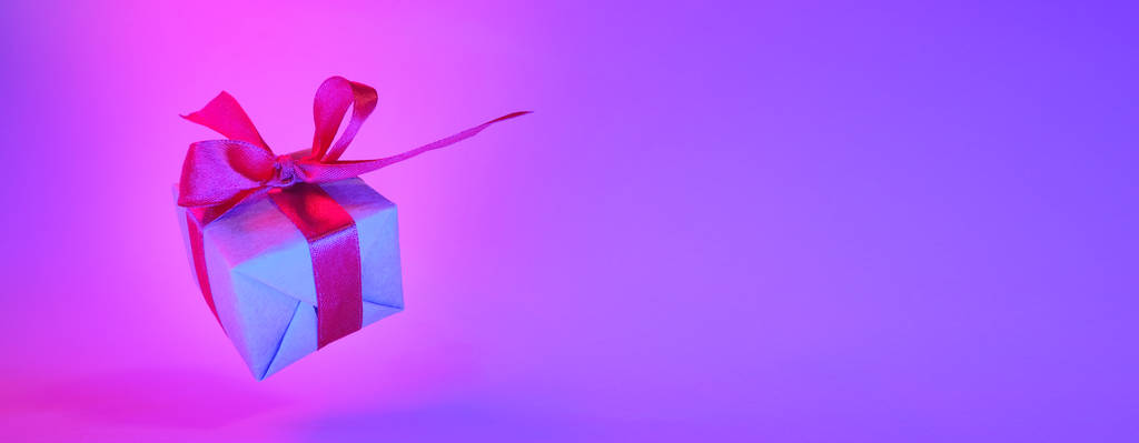 Caja de regalo con cinta roja sobre fondo de color neón de moda. bandera de gravedad cero. levitación. espacio de copia. Concepto de ventas, precio de descuento, regalos de Navidad y compras
 - Foto, imagen