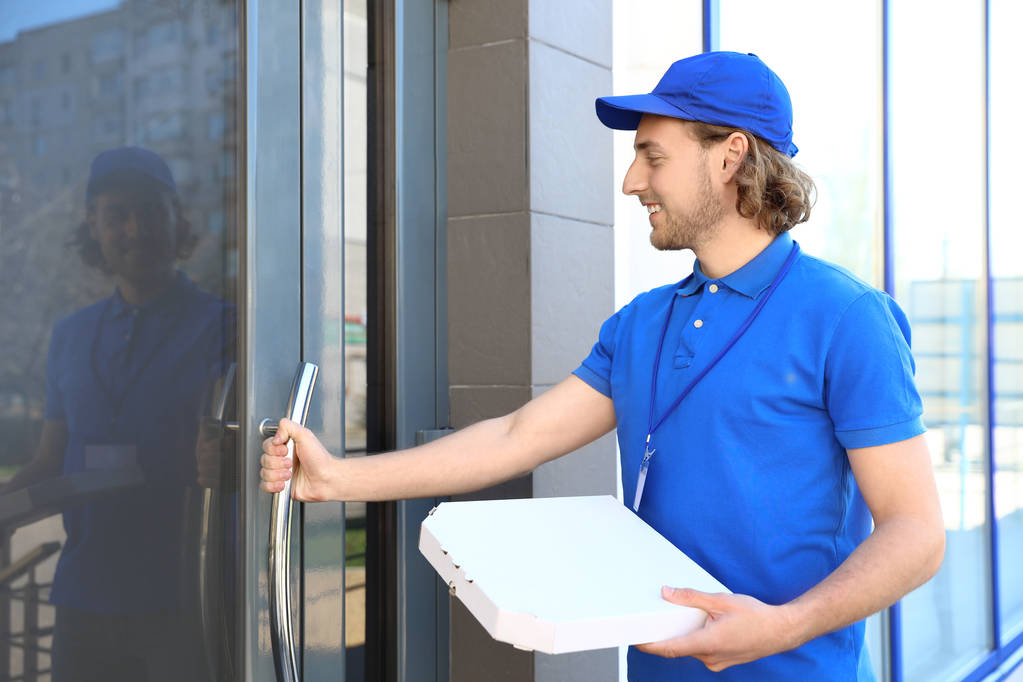 Correo masculino con pizza en la entrada. Servicio de entrega de alimentos
 - Foto, Imagen