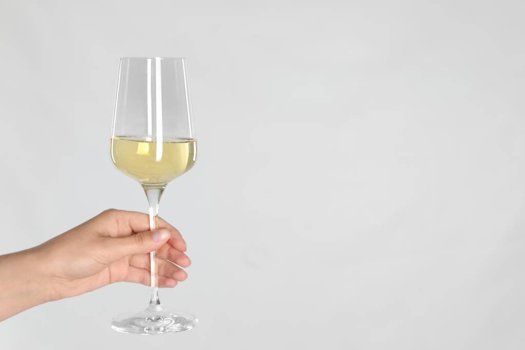 Жінка тримає келих білого вина на світлому фоні, крупним планом. Простір для тексту
 - Фото, зображення
