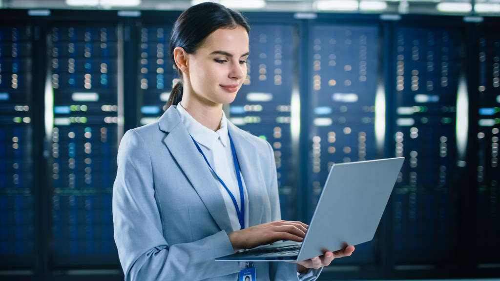 Жінка IT-спеціаліст працює на ноутбуці в центрі обробки даних поруч з серверними стелажами
. - Фото, зображення
