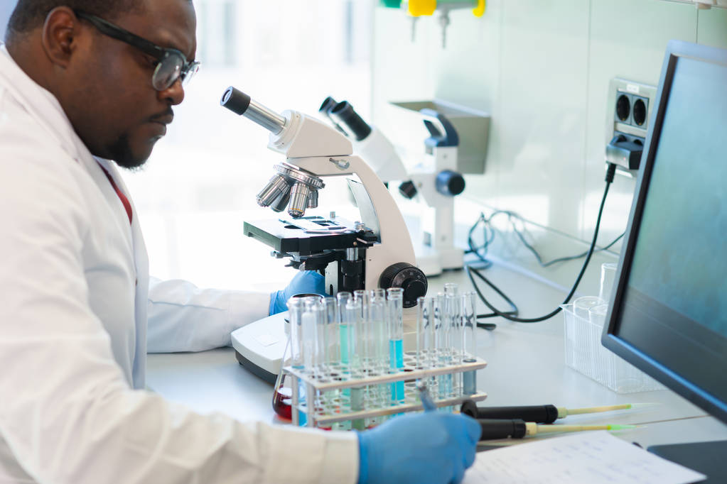 Laboratuvarda çalışan Afro-Amerikalı bir adam. Bilimadamı doktor tıbbi araştırma yapıyor. Laboratuvar aletleri: mikroskop, test tüpleri, ekipmanlar. Biyoteknoloji, kimya, bilim, deneyler ve sağlık hizmetleri. - Fotoğraf, Görsel