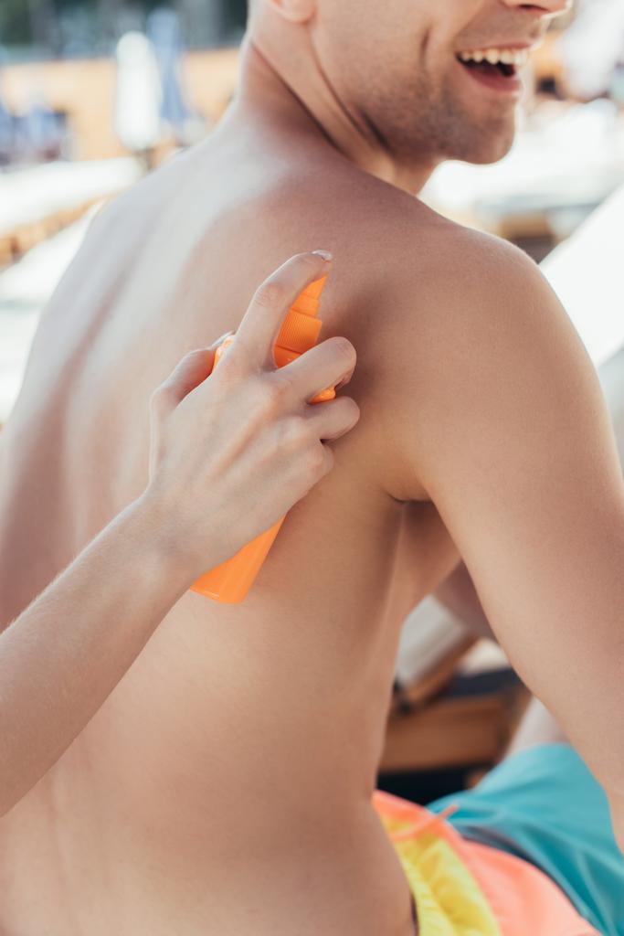 cropped view of woman applying sunscreen lotion on back of smiling boyfriend - Photo, Image