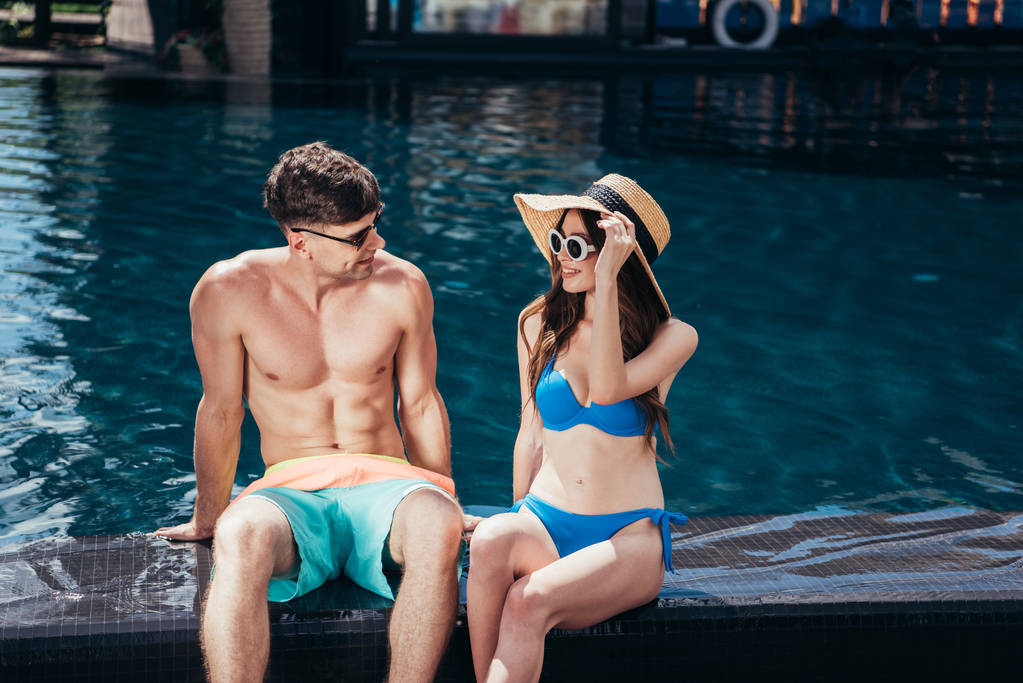 jeune couple souriant se regardant tout en étant assis près de la piscine
 - Photo, image