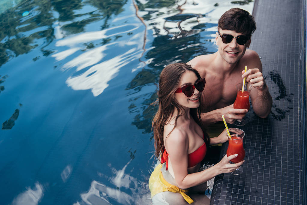 Veselý mladý pár s brýlemi osvěžující nápoje a s úsměvem na kameře - Fotografie, Obrázek