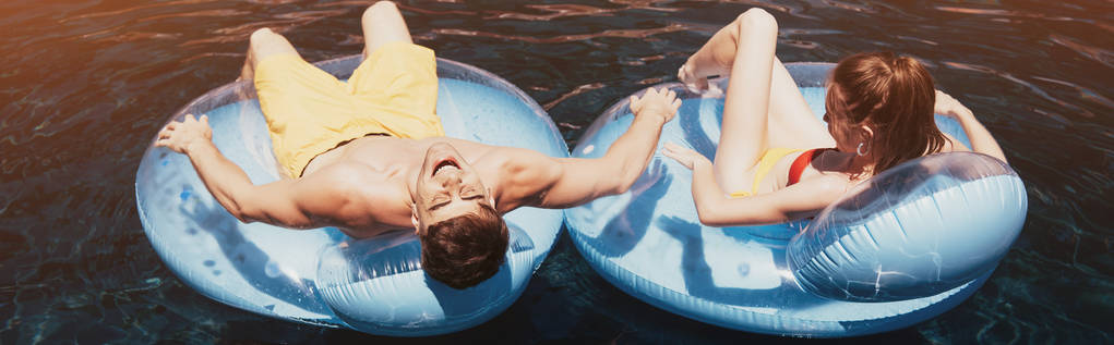 панорамний знімок молодої пари засмагає на плавальних кільцях у басейні
 - Фото, зображення