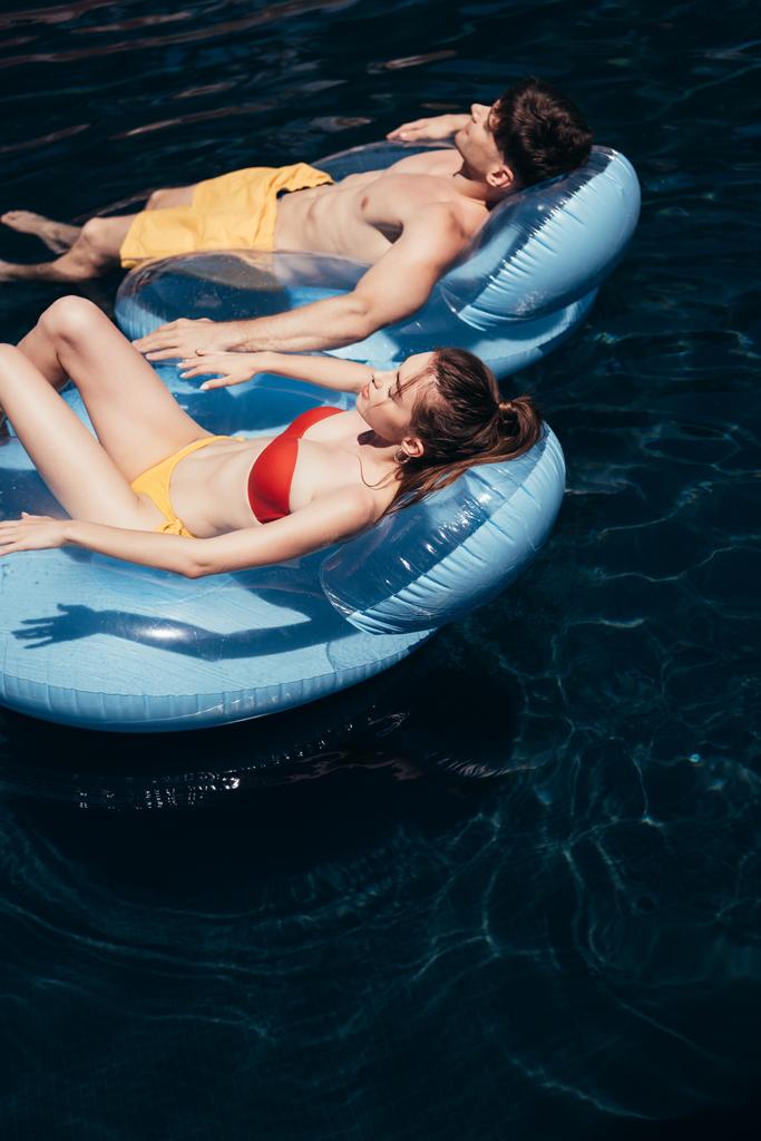 pareja joven tomando el sol mientras flota en los anillos de natación en la piscina
 - Foto, imagen