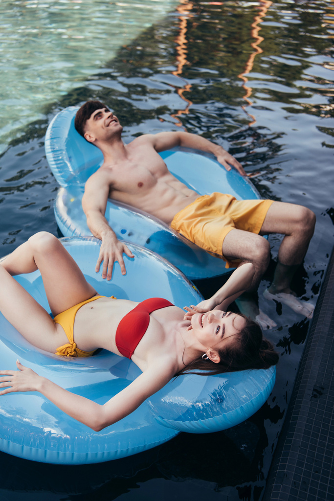 веселая молодая пара отдыхает на плавательных кольцах в бассейне и смотрит вверх
 - Фото, изображение