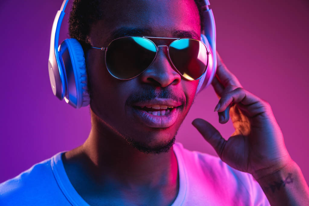 ネオンの光の中で音楽を聴く若いアフリカ系アメリカ人の男性 - 写真・画像