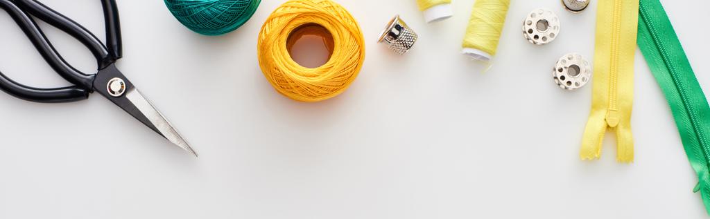 白い背景にハサミ、編み糸ボール、ジッパー、糸、ティンブルとボビンのパノラマショット  - 写真・画像