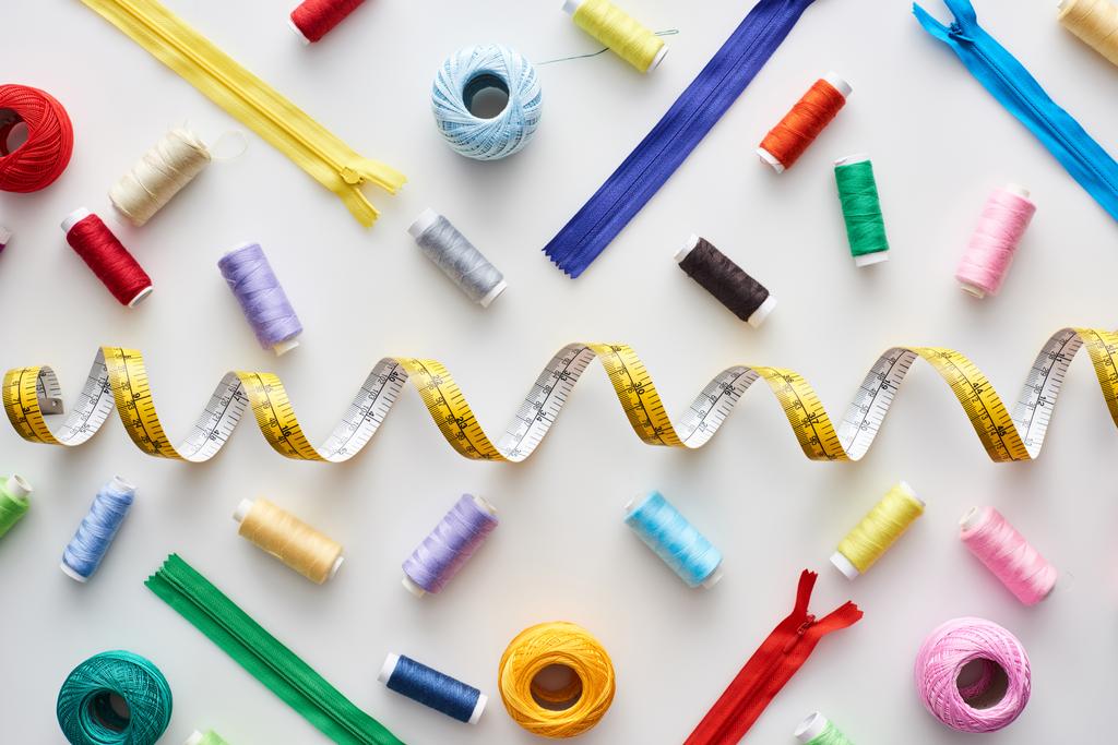 top view of measuring tape, colorful threads and zippers on white background  - Photo, Image