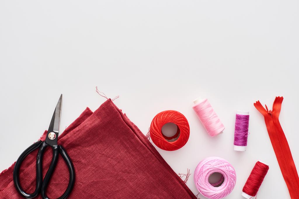 vue de dessus de fils colorés, boules de fils à tricoter, tissu, ciseaux et fermeture éclair sur fond blanc
  - Photo, image