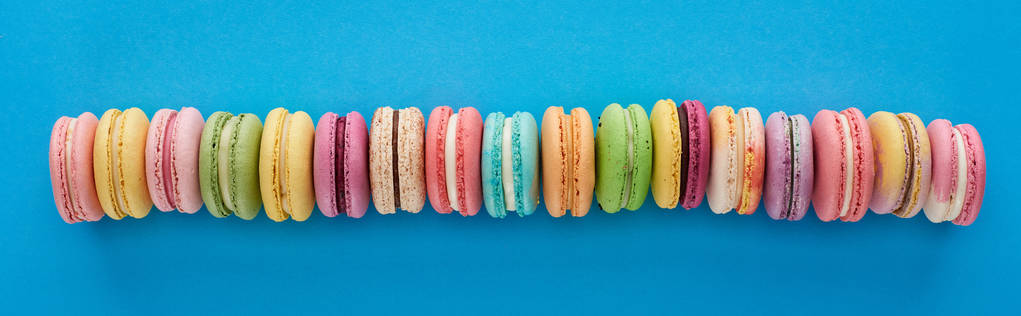 top view of multicolored delicious French macaroons in row on blue bright background, panoramic shot - Photo, Image