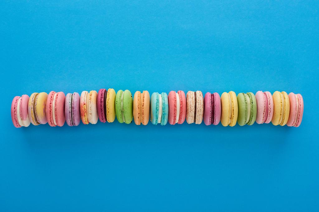 top view of multicolored delicious French macaroons in line on blue bright background with copy space - Photo, Image