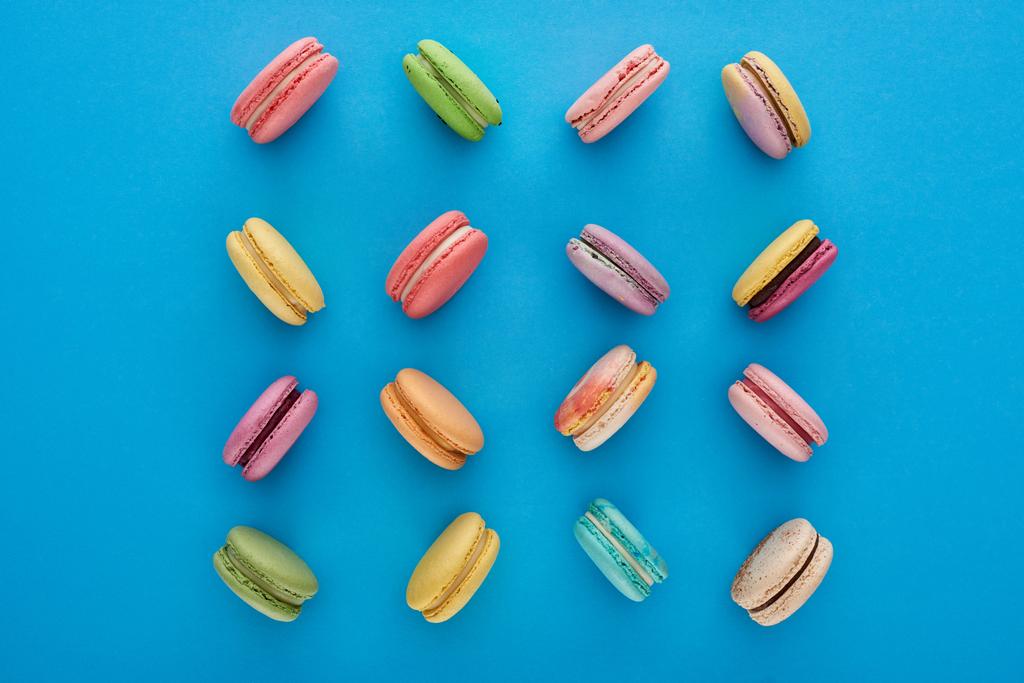 плоский з солодкими різнобарвними смачними французькими макаруни на синьому яскравому фоні - Фото, зображення