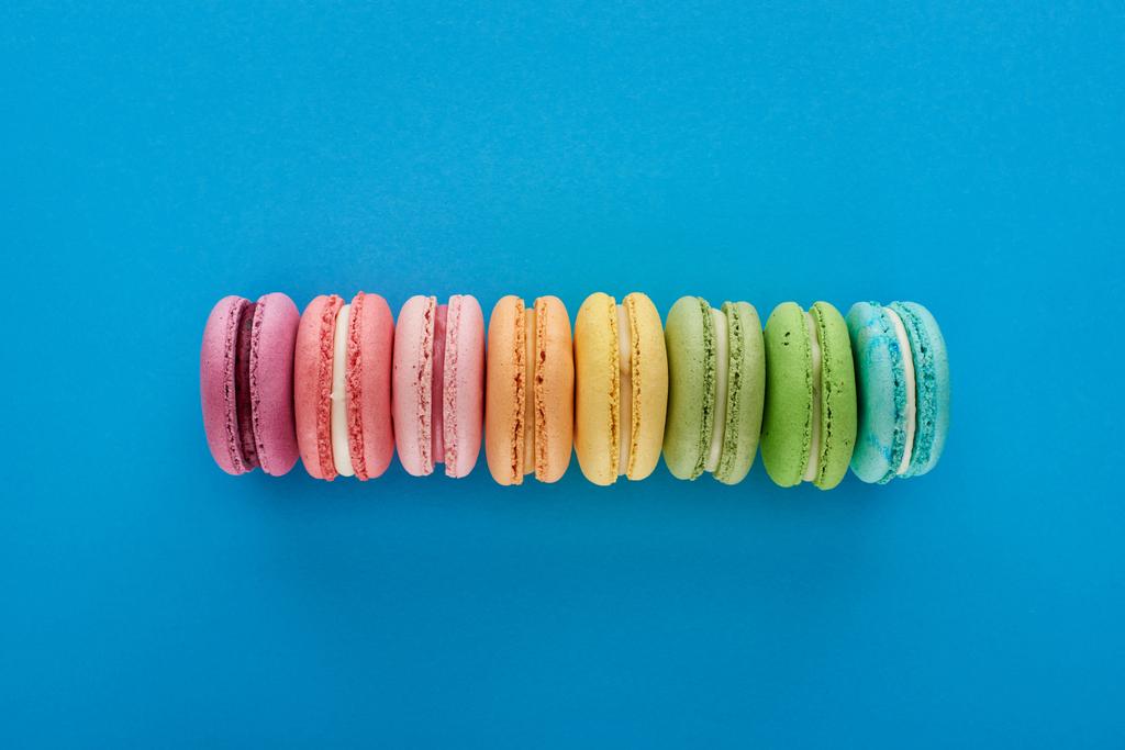 vista dall'alto di colorati macaron francesi freschi deliziosi in linea su sfondo blu brillante
 - Foto, immagini