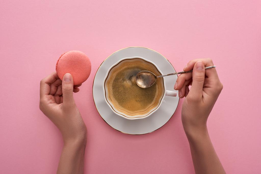 Teilweise Ansicht der Frau mit Löffel in der Nähe von Kaffee in Tasse und köstliche französische Makronen auf rosa Hintergrund - Foto, Bild