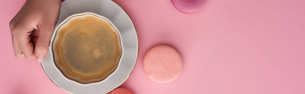 ピンクの背景においしいフランスのマカロンでコーヒーを飲んでいる女性のトリミングビュー、パノラマショット - 写真・画像