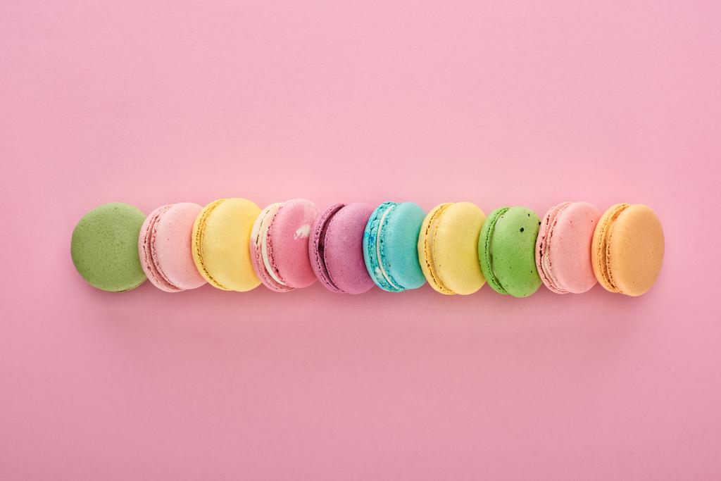 σειρά από νόστιμα πολύχρωμα γαλλικά αμυγδαλωτά διαφορετικών γεύσεων σε ροζ φόντο - Φωτογραφία, εικόνα