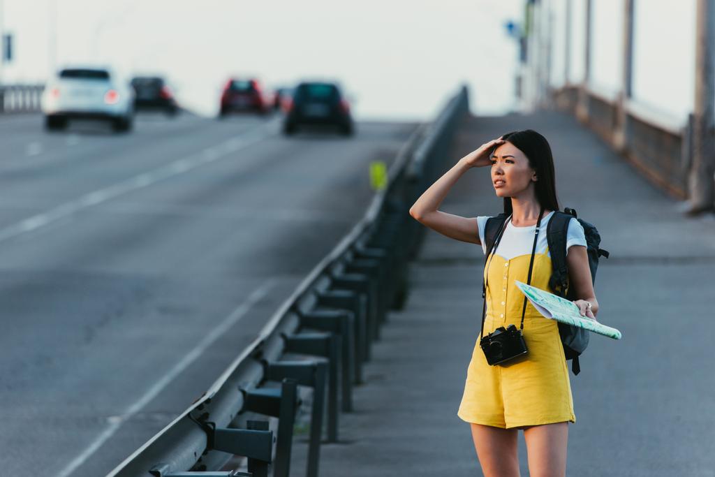 bezorgd en Aziatische vrouw in overalls houden kaart en op zoek weg  - Foto, afbeelding