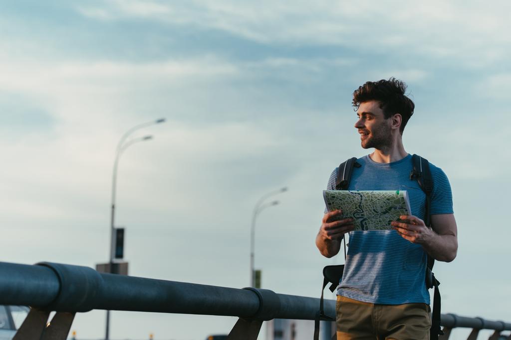 hombre sonriente y guapo en camiseta y pantalones cortos sosteniendo mapa y mirando hacia otro lado
  - Foto, Imagen