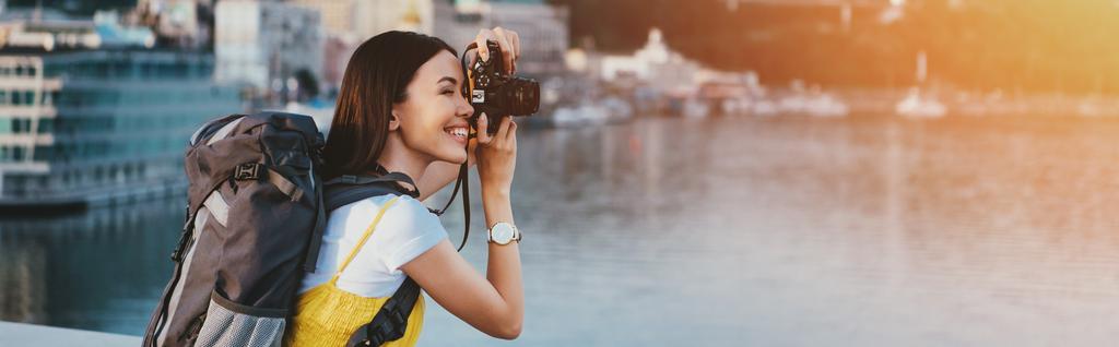 vista lateral da mulher asiática com mochila tirando foto
  - Foto, Imagem