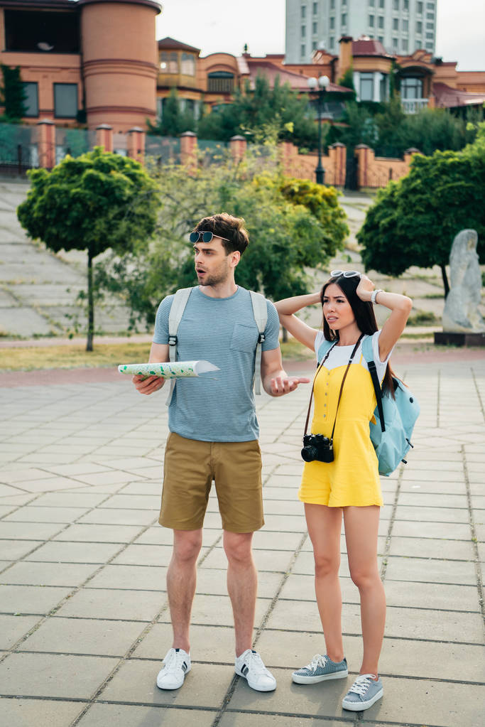 smutny i przystojny człowiek trzyma mapę i Asian kobieta patrząc od  - Zdjęcie, obraz