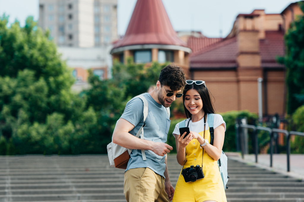 lächelnder und gutaussehender Mann und asiatische Frau, die auf ihr Smartphone schauen - Foto, Bild