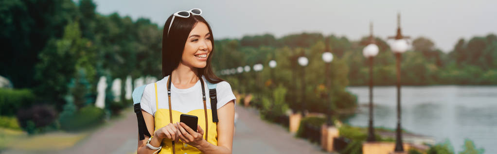 plano panorámico de mujer asiática y atractiva sosteniendo teléfono inteligente
 - Foto, imagen