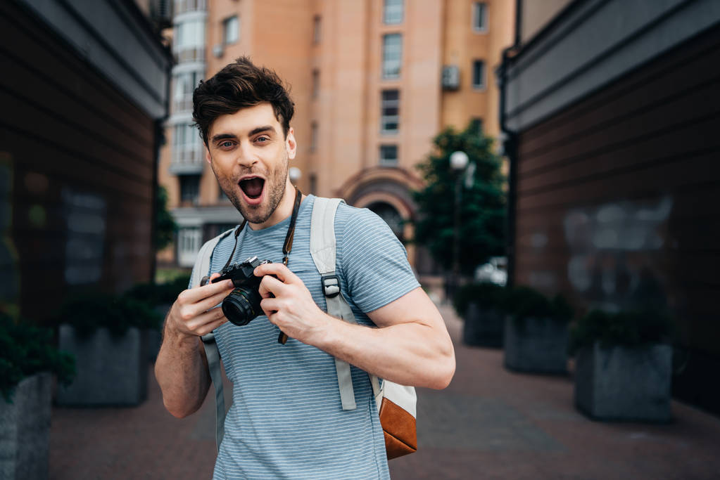 όμορφος άντρας με t-shirt κρατώντας ψηφιακή φωτογραφική μηχανή και κοιτάζοντας την κάμερα  - Φωτογραφία, εικόνα