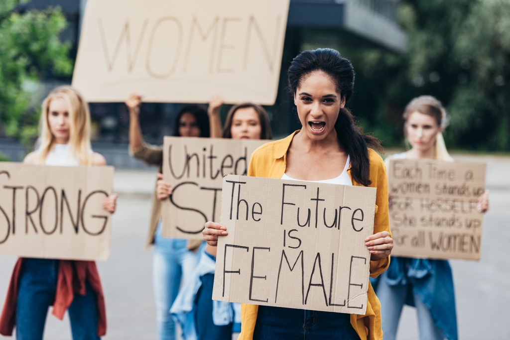vista frontal de gritando feminista afroamericana sosteniendo pancarta con inscripción el futuro es femenino en la calle
 - Foto, Imagen