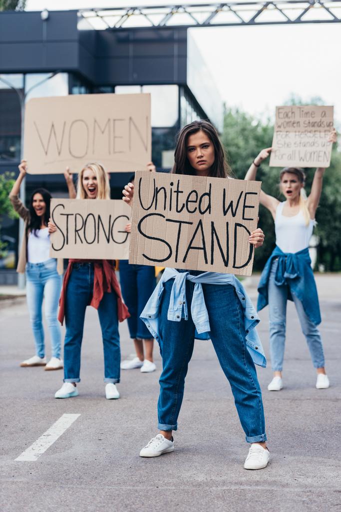 full length view of feminist holding placard with inscription united we stand near women on street - Photo, Image
